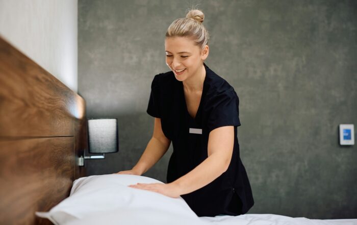 Happy maid changing bed linen in a room.